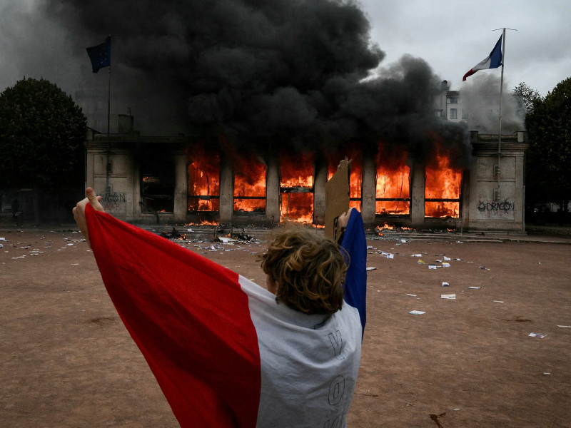 Un manifestante envuelto en la bandera nacional de Francia permanece frente a la oficina de turismo de Lyon, después de que el edificio fuera incendiado.